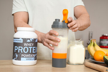 Sporty muscular man making protein shake at table in kitchen, closeup