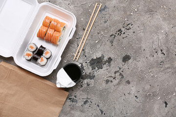 Plastic container with tasty sushi rolls, soy sauce and paper bag on grey grunge background....