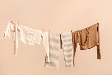 Different clothes hanging on rope against color background