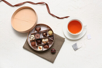 Box with candies, cup of tea and tea bag on light background