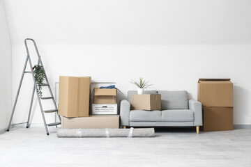 Grey sofa and cardboard boxes near white wall in light living room on moving day