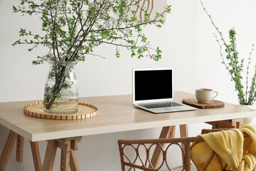 Stylish workplace, armchair, laptop and vase with blossoming branches in light living room