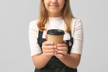 Teenage barista with takeaway cup of coffee on grey background, closeup