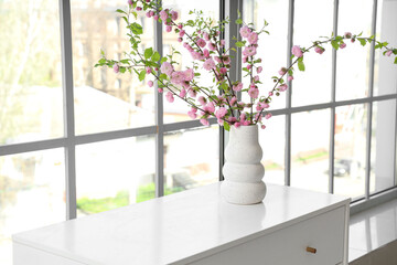 Vase with beautiful blooming branches on table in room