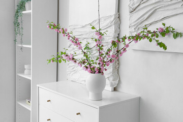 Vase with blooming branches on chest of drawers in room
