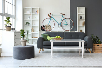 Interior of stylish living room with black sofa, coffee table, bicycle and shelving unit