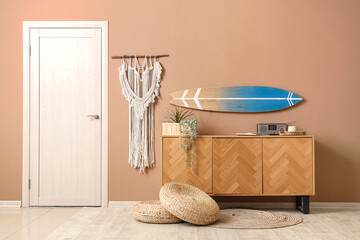 Chest of drawers, houseplant and surf board on beige wall in stylish room
