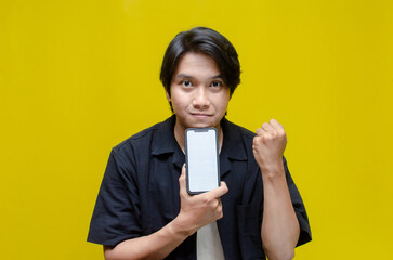 mock up young Asian man showing and pointing at blank screen smartphone. asian man in beige tshirt...