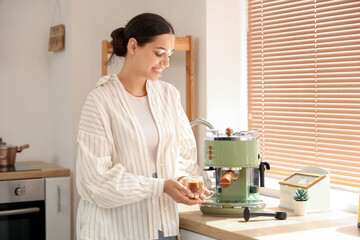 Beautiful young happy woman cup of cappuccino and modern coffee machine in kitchen