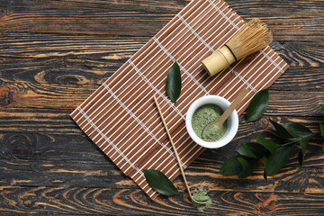 Bowl of matcha powder with chasen and chashaku on wooden background