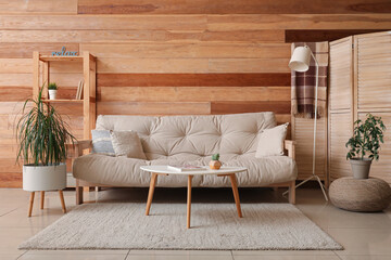 Interior of living room with cozy sofa, coffee table, lamp and folding screen near wooden wall