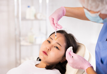 Closeup face of young female client receiving injections during lip enhancement procedure,...