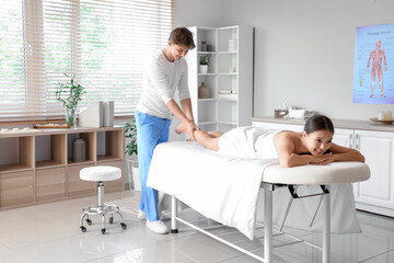 Male therapist massaging young woman's leg in spa salon