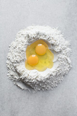 Overhead view of eggs and flour on a marble countertop, eggs and flour being mixed to make homemade egg noodles and pasta, process of making fresh egg noodles