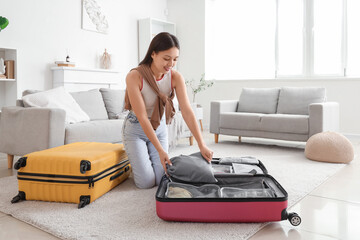 Young Asian woman packing organizer into suitcase at home. Travel concept