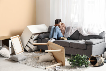 Young woman sitting on sofa in messed living room after earthquake