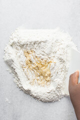 Overhead view of egg noodles dough being mixed on a marble countertop, eggs and flour being mixed to make homemade egg noodles and egg pasta, process of making fresh egg noodles