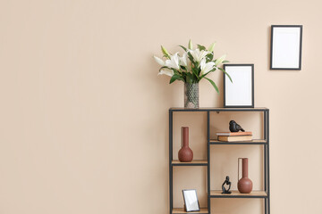 Shelving unit with vase of lily flowers and photo frames near beige wall in room