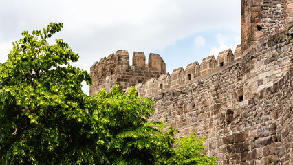 Kayseri citadel. Close-up view of the ancient stone fortress walls with lush green trees in the foreground and a partly cloudy sky above. Kayseri, Cappadocia, Turkey (Turkiye)