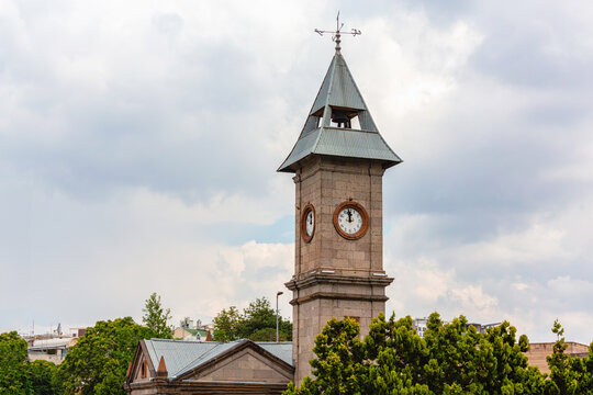 Picturesque clock tower in Kayseri, Turkey, set against a cloudy sky with lush greenery in the foreground. Kayseri, Turkey (Turkiye)