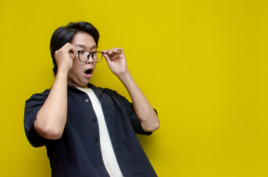 funny expression young asian man shocked happily opening mouth and lowering glasses. asian man with glasses feels shock with wow surprised expression.