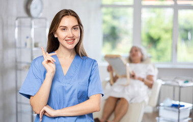 Friendly young female medical person standing in treatment room of aesthetic center