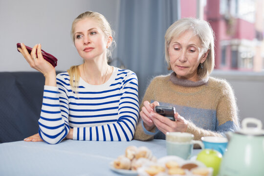 Mature woman and her adult daughter are sitting at a table with mobile phones, talking to someone on speakerphone