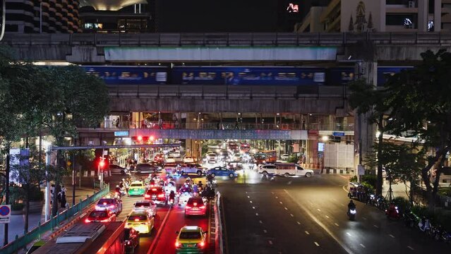 Vibrant night traffic on Bangkok city streets with moving skytrain and vehicles