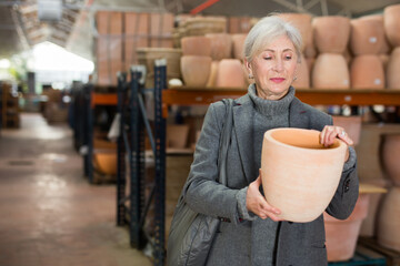 Elderly caucasian woman shopping in crockery store and choosing earthenware pot.