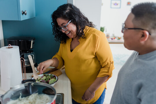 Latin lesbian couple cooking dinner at home in Mexico, Hispanic homosexual people from lgbt community with rainbow flag in Latin America