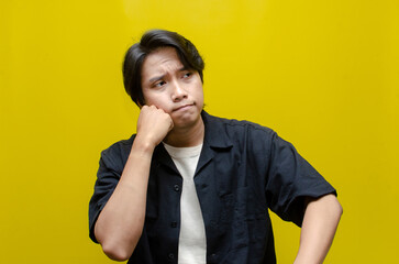 a young asian man touching his chin as a gesture of thinking with thoughtful expression. asian man...