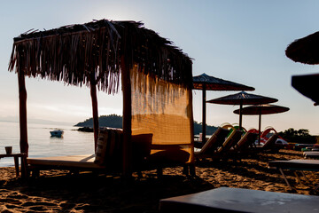 Straw umbrellas and sunbeds on the beach against the background of the sea at dawn. Relaxing...