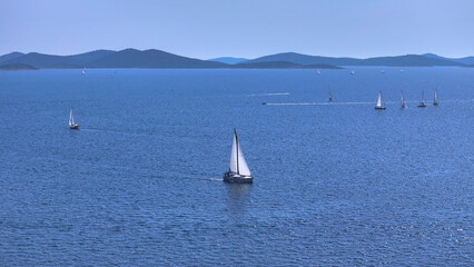 AERIAL: Countless sailboats sail the deep blue seas on a sunny summer day.