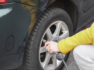 The hands of a man pump air into the wheel of the car with a compressor.