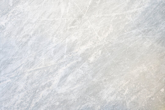 Icy background on rink reveals visible traces of skating, capturing the essence of winter sport. Texture of ice on skating rink is apparent from a top view, showcasing sheet of scratched ice.
