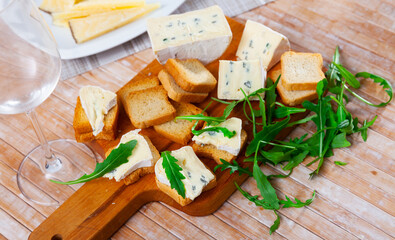 Sliced blue cheese served on board with toast and arugula to table