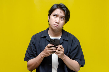 an overthinker young Asian man in pensive mood holding phone with sad and thoughtful expression....