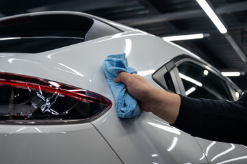 A mechanic wipes the body of a white car with a microfiber cloth. 