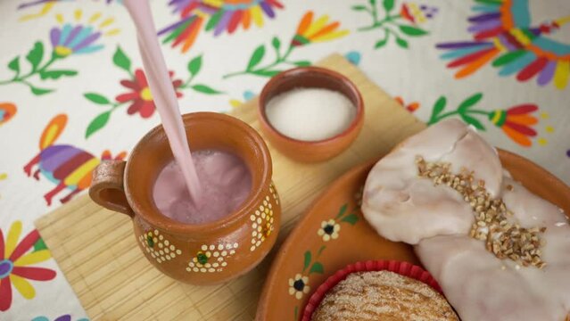 Pouring strawberry atole into a clay jar, lots of foam