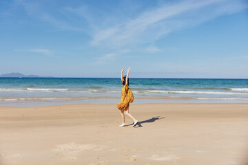 Woman in yellow dress standing on beach with arms outstretched in peaceful and serene pose against...