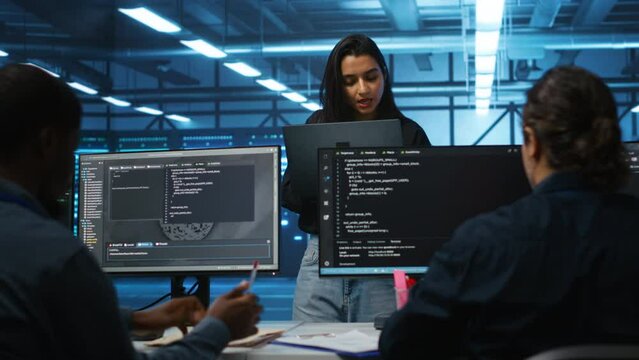 Portrait of smiling Indian manager in server room managing team of engineers looking for equipment misconfigurations. Happy team leader coordinating employees checking data center bottlenecks