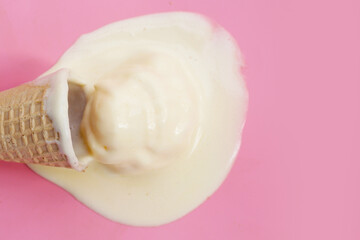 Melting ice cream ball with waffle cone on pink background.