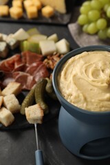 Fondue with tasty melted cheese, fork and different snacks on black table