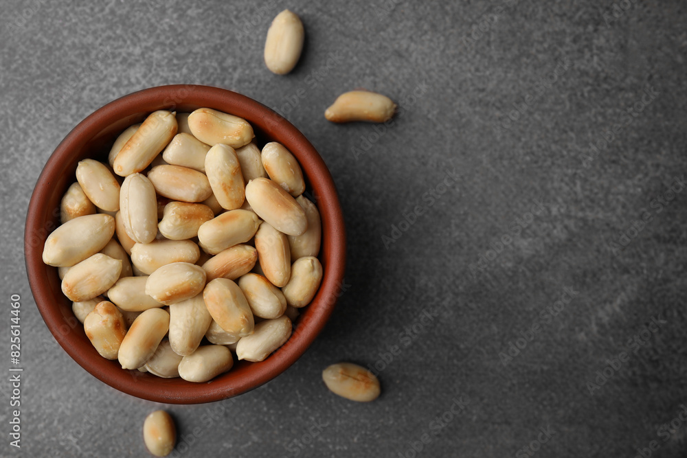 Poster Roasted peanuts in bowl on brown table, top view. Space for text