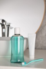 Bottle of mouthwash, toothpaste and toothbrush on light countertop in bathroom