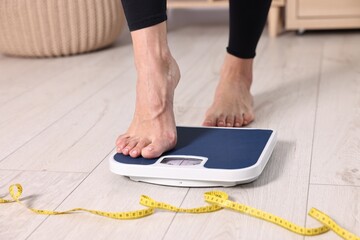 Woman stepping on floor scale and measuring tape at home, closeup. Weight control