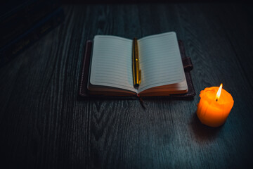 A notebook with a gold pen on the table in the candlelight