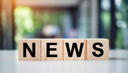 Wooden blocks spell "NEWS" on a white table, with a blurred newsroom background, symbolizing communication, media, and information dissemination