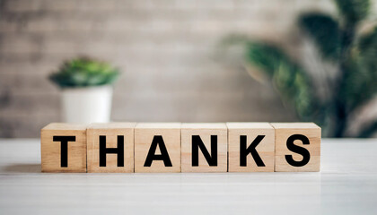 Wooden blocks spell "THANKS" on a white table with a blurred background, symbolizing gratitude, appreciation, and acknowledgment in a simple and heartfelt manner