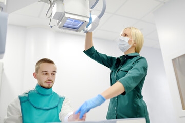 Female radiologist going to made x-ray shot of young man hand in x-ray room in modern clinic....